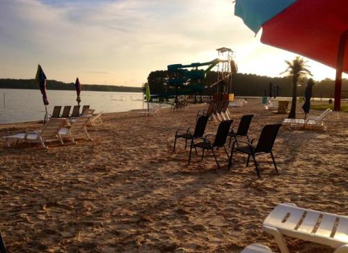 A sandy beach with lounge chairs, colorful umbrellas, and a water slide in the background under a sunset sky.