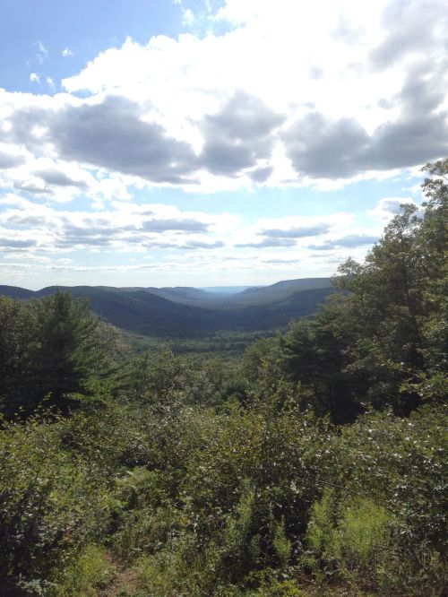 A scenic view of a lush green valley surrounded by mountains under a partly cloudy sky.