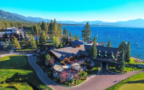 Aerial view of a lakeside resort with a restaurant, surrounded by trees and mountains, overlooking a blue lake.