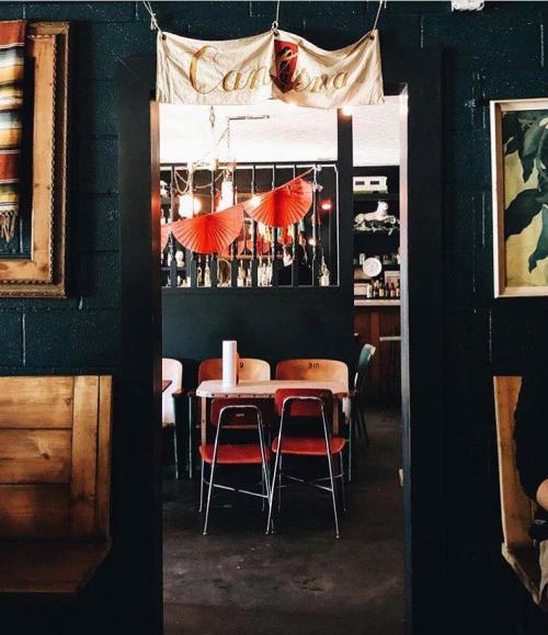 A cozy restaurant interior featuring a table with red chairs, decorative fans, and a banner reading "Cantina."