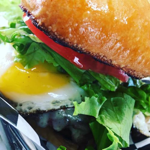 A close-up of a burger with a shiny bun, lettuce, tomato, and a fried egg, showcasing fresh ingredients.