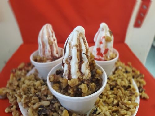 Three ice cream cones topped with chocolate syrup and cherries, surrounded by a pile of chopped walnuts.