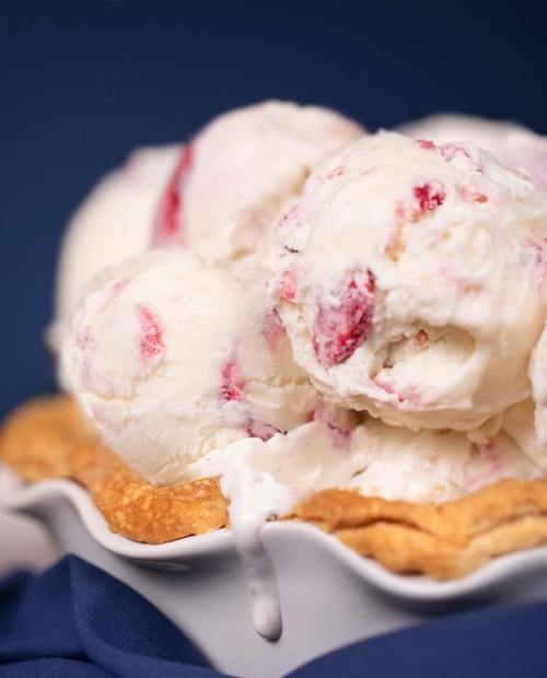 A close-up of scoops of strawberry ice cream melting over a flaky pie crust in a white dish.