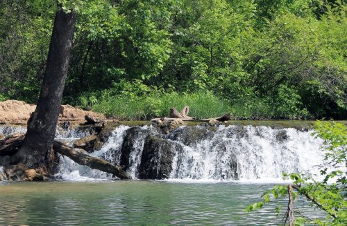 A serene waterfall cascades over rocks, surrounded by lush green trees and foliage.