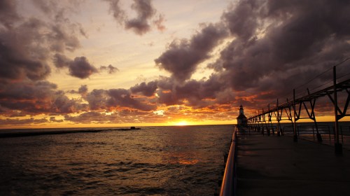 A scenic sunset over the ocean, with dramatic clouds and a pier extending into the water.