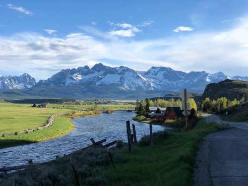Scenic view of mountains with snow caps, a river, and a rural landscape under a clear blue sky.