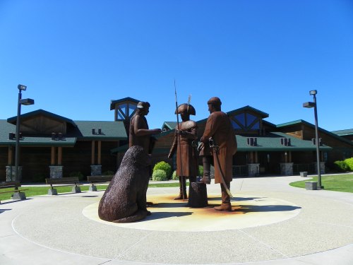 A bronze sculpture of three figures and a bear, set in a circular plaza with a building in the background under a clear blue sky.