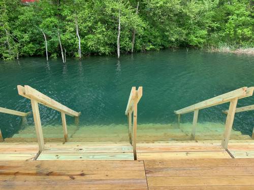Wooden steps lead down to a calm, greenish-blue body of water surrounded by lush greenery.