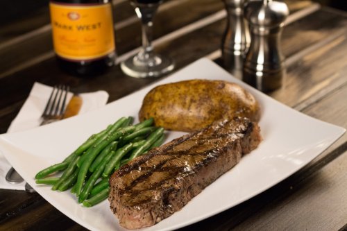 A plate with grilled steak, green beans, and a baked potato, accompanied by a glass of red wine and a bottle in the background.