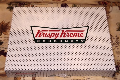 A white box with black polka dots featuring the Krispy Kreme logo and the word "DOUGHNUTS."