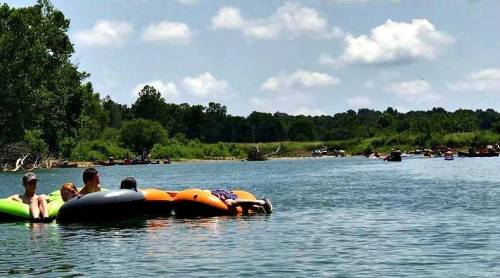 A group of people floating on colorful inner tubes in a calm river, surrounded by greenery and a clear blue sky.
