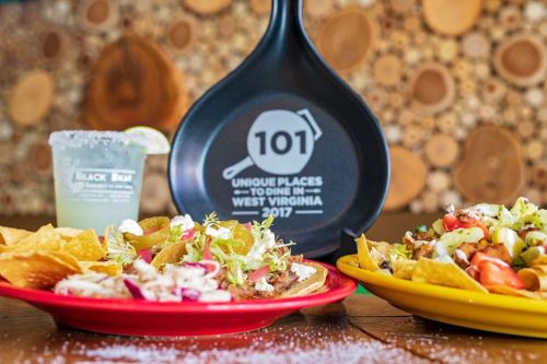 A vibrant spread of tacos and nachos with a drink, set against a rustic wooden backdrop and a promotional sign.