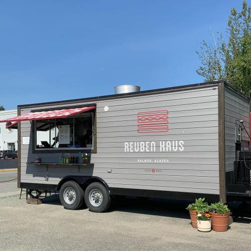 A food truck named "Reuben Haus" in Palmer, Alaska, with a red awning and potted plants outside.