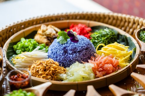 A colorful platter of rice and various vegetables, featuring blue rice at the center, garnished with herbs and flowers.