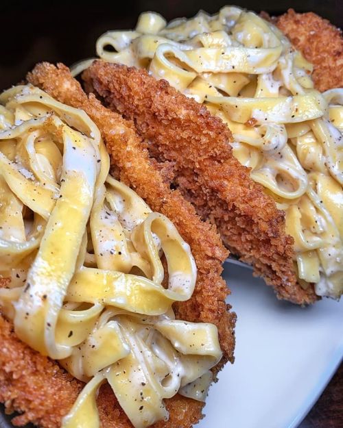 Crispy fried chicken cutlets filled with creamy fettuccine alfredo pasta, garnished with black pepper.