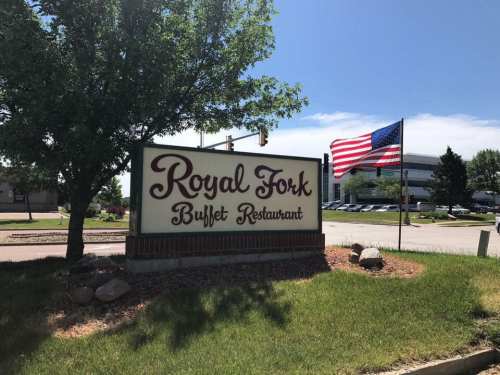 Sign for Royal Fork Buffet Restaurant with an American flag and greenery in the background on a sunny day.