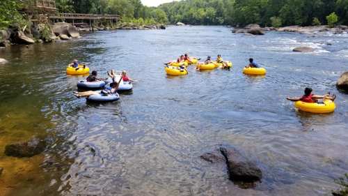A group of people floating on yellow and blue inner tubes in a river surrounded by trees and rocks.