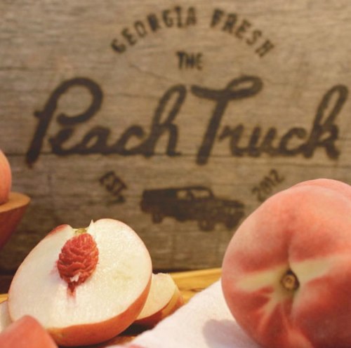 Fresh peaches and a sliced peach in front of a rustic sign for "The Peach Truck" from Georgia.