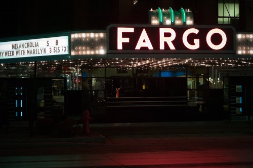 Neon-lit Fargo theater marquee at night, featuring movie titles and a classic art deco design.