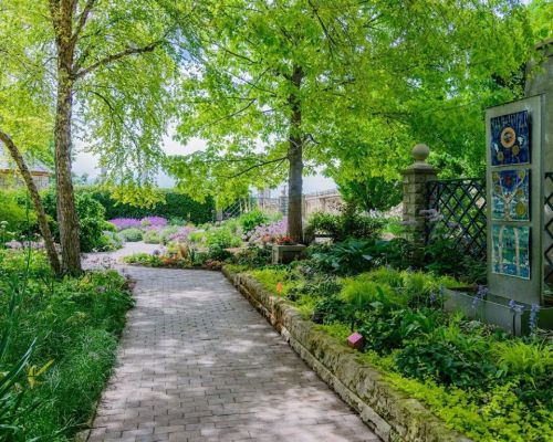 A serene garden path lined with vibrant flowers and lush greenery, leading through a peaceful landscape.
