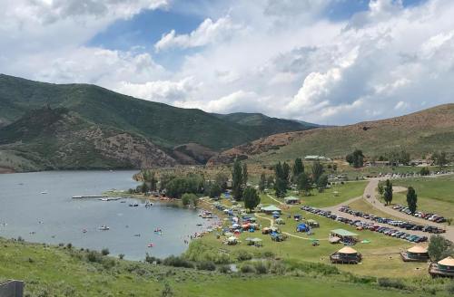 A scenic view of a lake surrounded by green hills, with people enjoying the beach and parked cars along the shore.