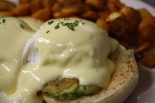 A close-up of eggs Benedict with poached eggs and hollandaise sauce on an English muffin, served with golden potatoes.