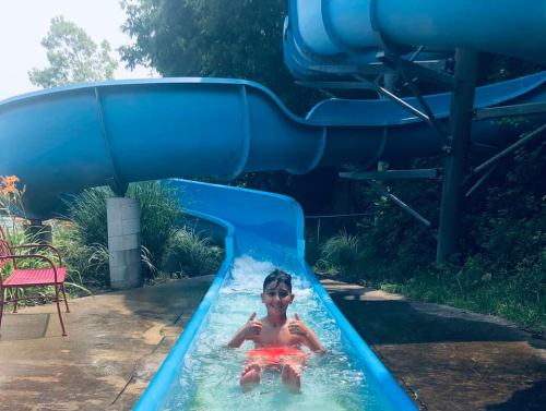 A child in a red swimsuit gives a thumbs-up while sliding down a blue water slide.
