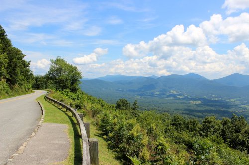 Scenic mountain view from a roadside overlook, featuring lush greenery and a clear blue sky with fluffy clouds.