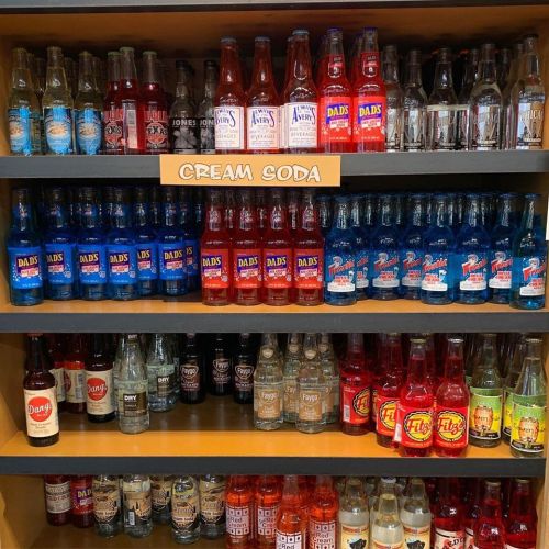 A shelf filled with various colorful soda bottles, labeled "Cream Soda" at the top.