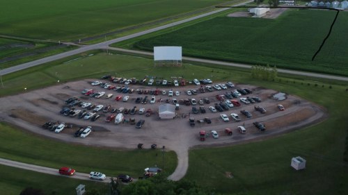 Aerial view of a drive-in movie theater with parked cars arranged in a circular layout and a large screen in the background.