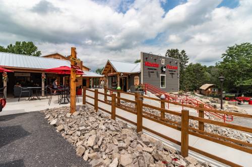 A scenic view of a rustic outdoor area with buildings, seating, and a pathway lined with rocks under a cloudy sky.