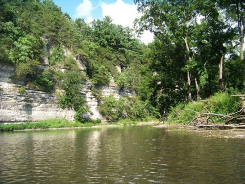 A serene river scene with lush greenery and steep cliffs under a clear blue sky.