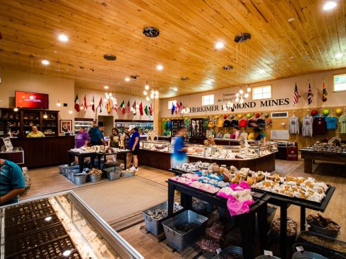 A bustling gift shop with displays of minerals and souvenirs, featuring a wooden ceiling and flags from various countries.