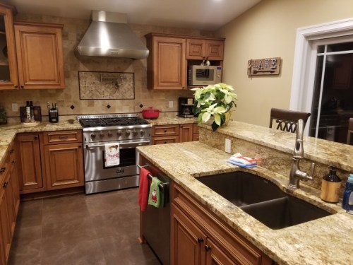 A modern kitchen with wooden cabinets, granite countertops, a large stove, and a sink, featuring decorative plants.