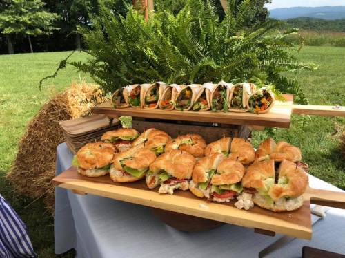 A wooden display of croissant sandwiches and fresh vegetable wraps on a grassy outdoor setting.
