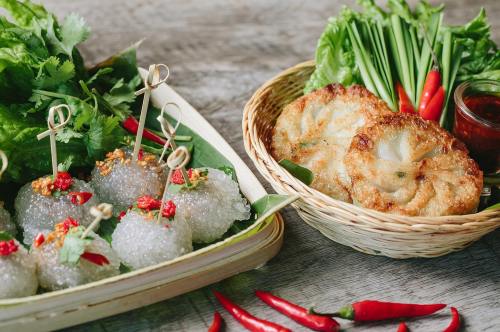 A bamboo basket with crispy snacks and a plate of glutinous rice balls garnished with herbs and red chilies.