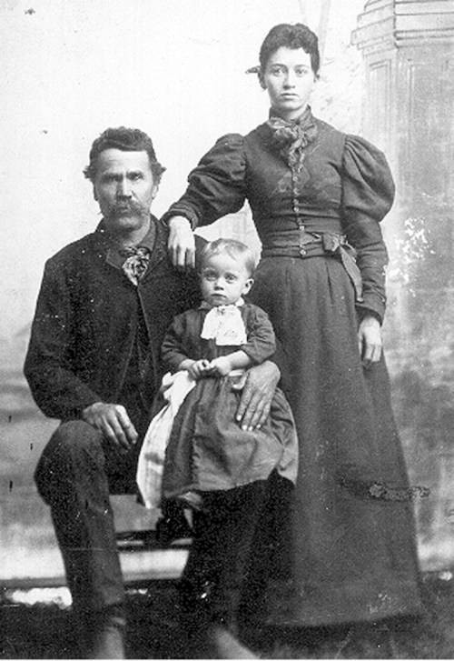 A vintage black-and-white photo of a man, woman, and child posing together, dressed in 19th-century clothing.
