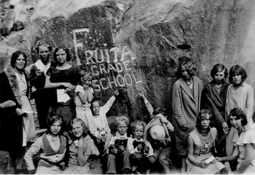 Black and white photo of a group of children and adults in front of a rock with "Fruita Grade School" carved into it.