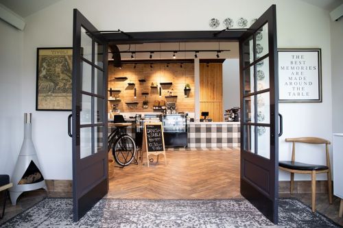 A cozy café entrance with open doors, featuring wooden decor, a coffee counter, and a welcoming atmosphere.