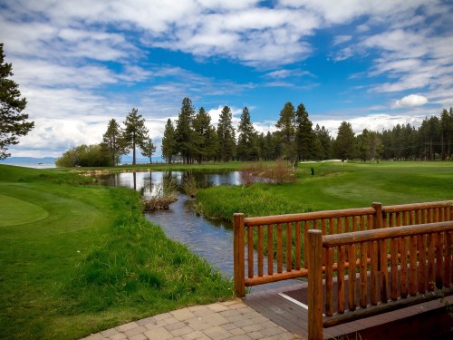 A serene golf course scene featuring a stream, lush greenery, and a blue sky with clouds.