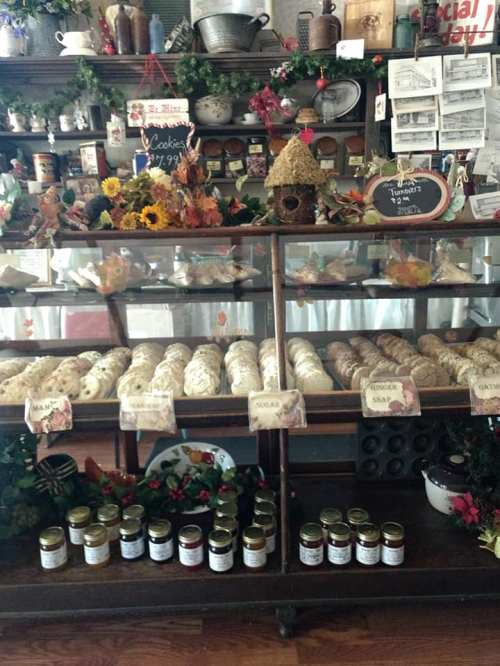 A display of assorted cookies and jars of preserves on a wooden shelf, decorated with autumn-themed decor.
