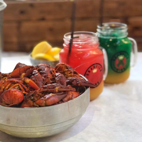 A bowl of cooked crawfish with lemon slices and two colorful drinks in mason jars.