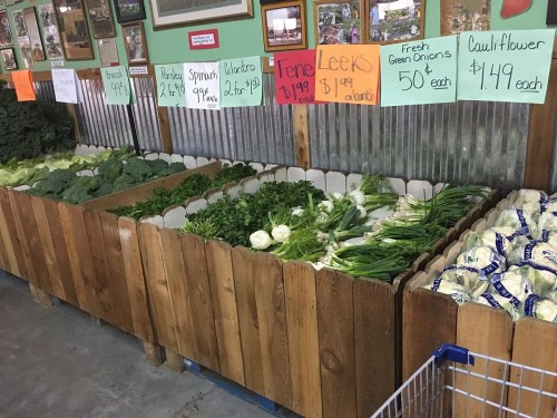 A display of fresh vegetables including broccoli, spinach, leeks, green onions, and cauliflower in wooden bins.