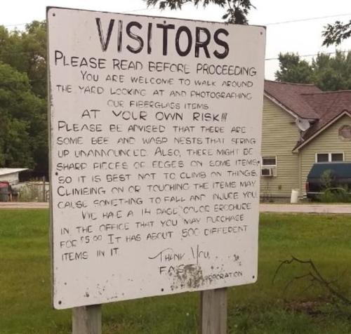 A sign warning visitors about risks in the yard, including bees and sharp objects, and advising caution while exploring.