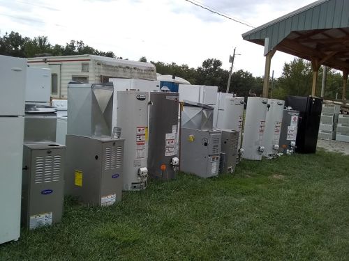 A row of various appliances, including refrigerators and water heaters, lined up on grass under a shelter.