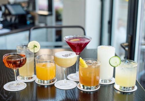 A variety of colorful cocktails arranged on a table, featuring garnishes like lemon, cucumber, and lavender.