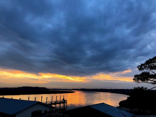 A serene sunset over a calm river, with dark clouds and vibrant orange hues reflecting on the water's surface.