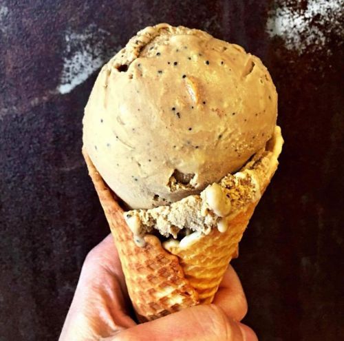 A hand holding a cone filled with creamy coffee-flavored ice cream, with a textured brown background.