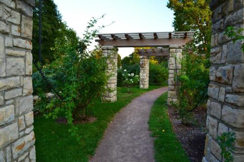 A stone pathway leads through a garden with columns and greenery, creating a serene outdoor space.
