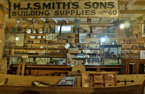 Interior of a vintage store displaying building supplies, antiques, and historical items on wooden shelves.